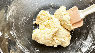 ホットケーキミックスを加え、ヘラで粉っぽさがなくなるまで混ぜている