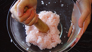 すりこぎを水で濡らし、もち米の粒が半分残る程度につぶしている
