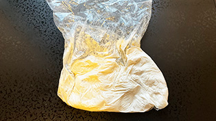 バナナのビニール袋の方へ潰した白玉粉を加え、水を少量ずつ加えて混ぜ、耳たぶ位のかたさになるまで練っている