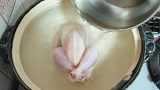 鶏のお腹を上にして土鍋に入れ、ひたひたの水を加えているところ