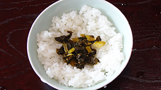お醤油をからませた刻み高菜をご飯にのせて指先で茶碗の縁から浮かせるる