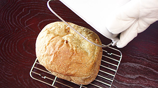 焼き上がりのブザーが鳴ったのでミトンをはめてパンを取り出し、足付き網の上に置いている