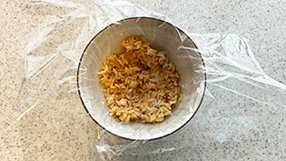 お茶碗にラップを敷き、ご飯の1/4を入れて均等にならしている