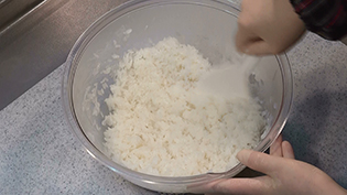 炊き立てのご飯をボウルに移し、合わせ酢を入れてしゃもじで切るように混ぜている