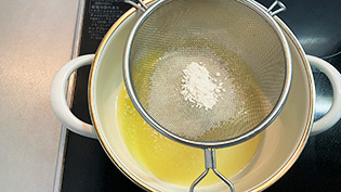 鍋にバターを入れて弱火にかけ、バターが溶けたら火を消して、薄力粉をふるいにかけながら加えている