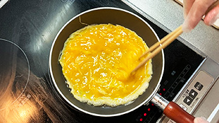 フライパンに油を熱し、菜箸で全体を混ぜて卵をふんわりとさせ、半熟状に焼いている