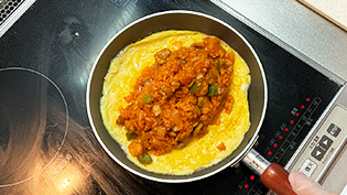 火を止め、チキンライスを一の字を書くように卵焼きの中心にのせて包む