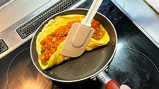卵の端をゴムベラではがし、チキンライスごとフライパンの奥に寄せるようにして包んでいるところ
